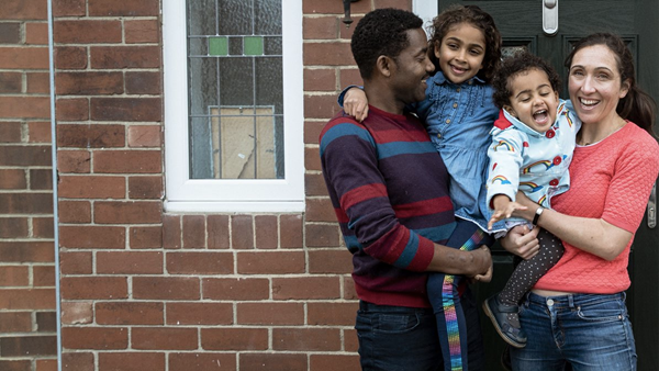 Young family standing together with their children, smiling on their front doorstep