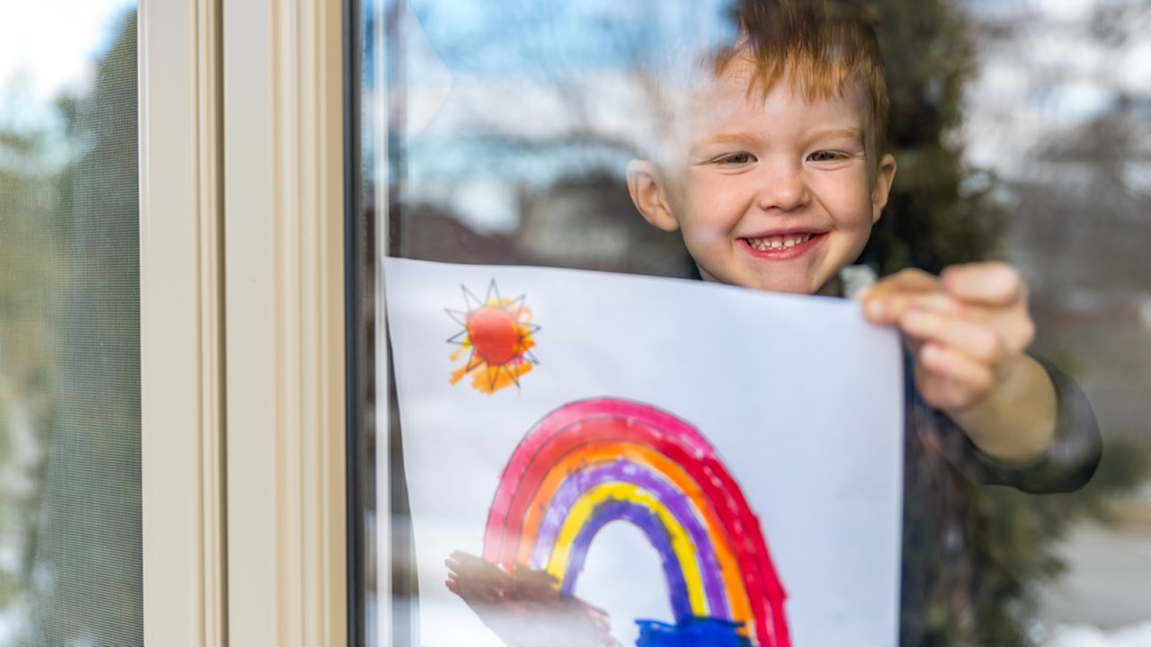 Child at window holding rainbow drawing