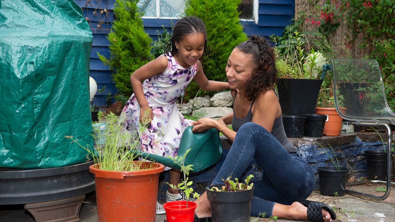 Mother and daughter outdoors watering plants.
